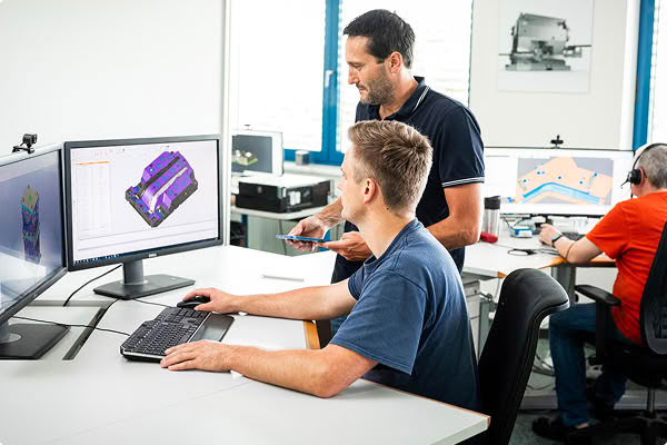 Ingenieure arbeiten gemeinsam an Computerarbeitsplätzen, um technische Entwürfe und Produktionsdaten eines Spritzgusswerkzeugs zu überprüfen.