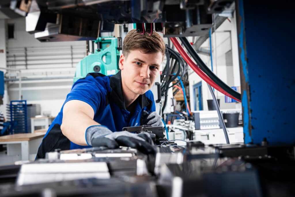 Techniker in blauem Arbeitshemd bei der Einstellung von Industrieanlagen an einer Produktionslinie.