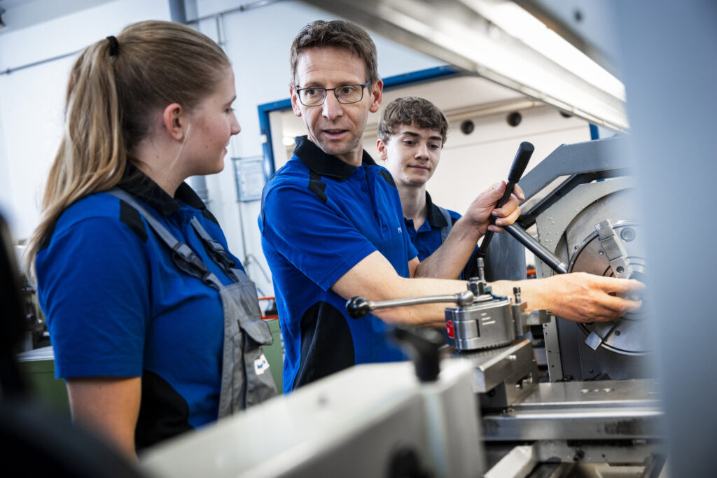Instructor explains a lathe to two apprentices