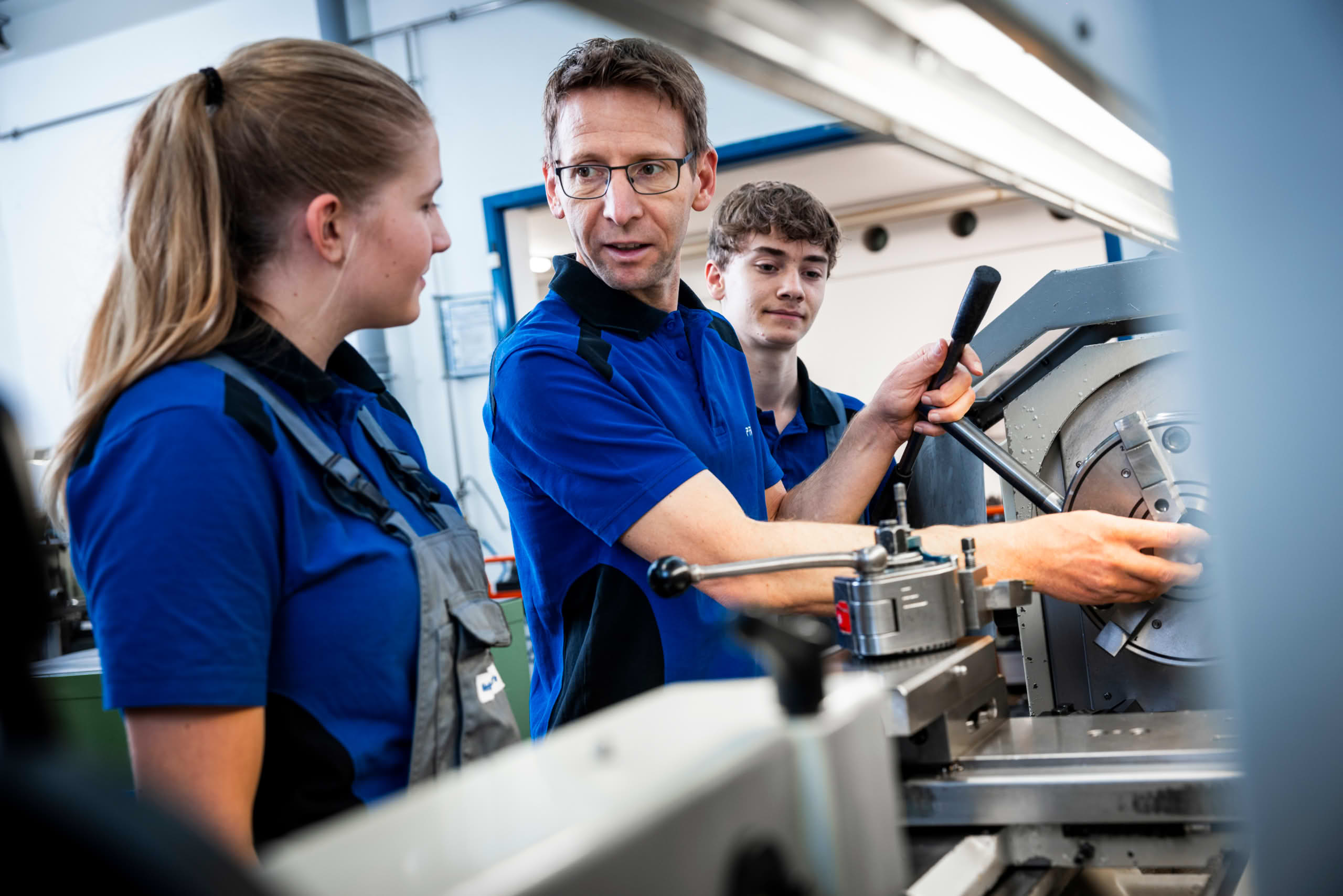 Instructor explains a lathe to two apprentices