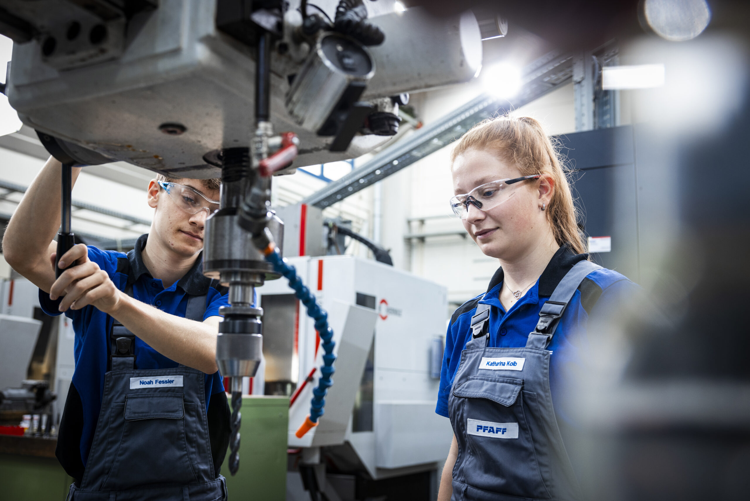 Two apprentices with safety glasses at a milling machine