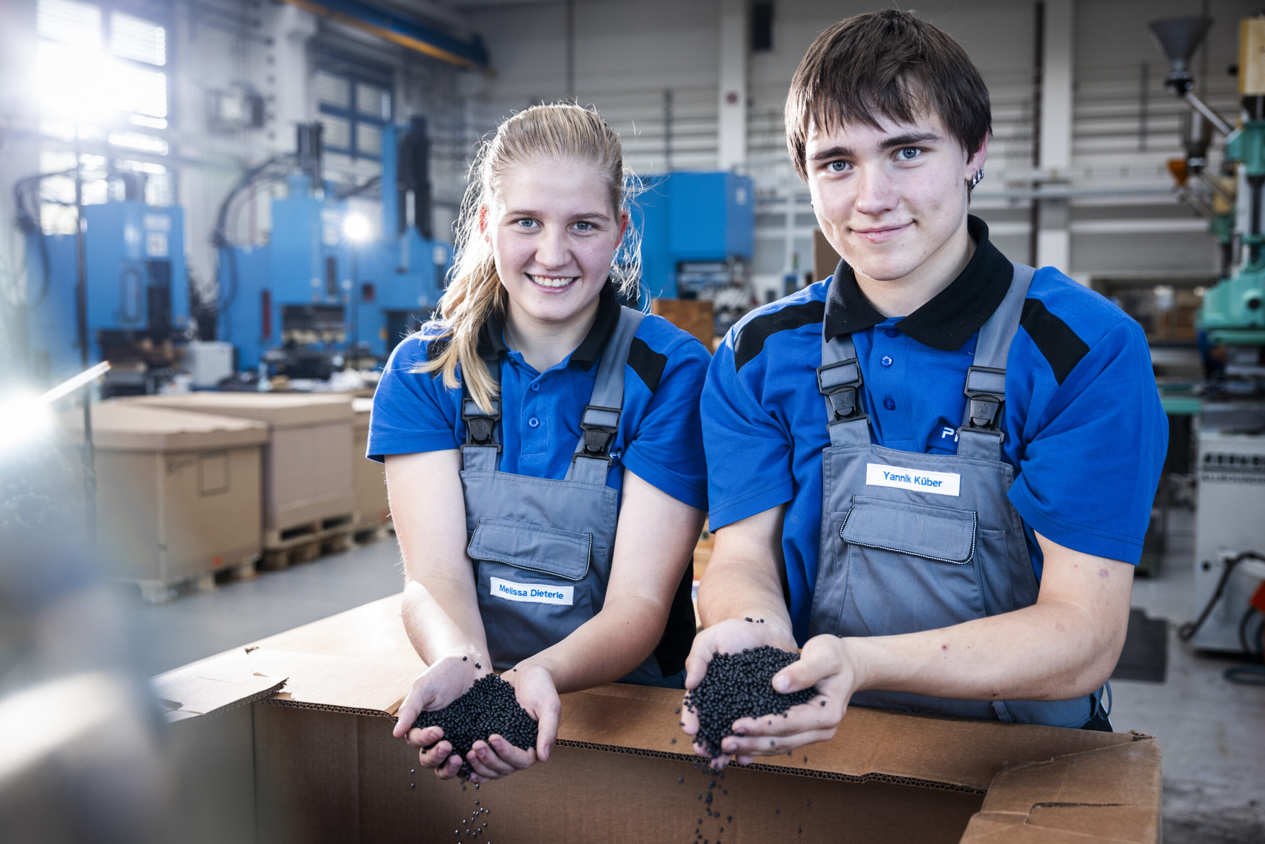 Two apprentices hold plastic components in production