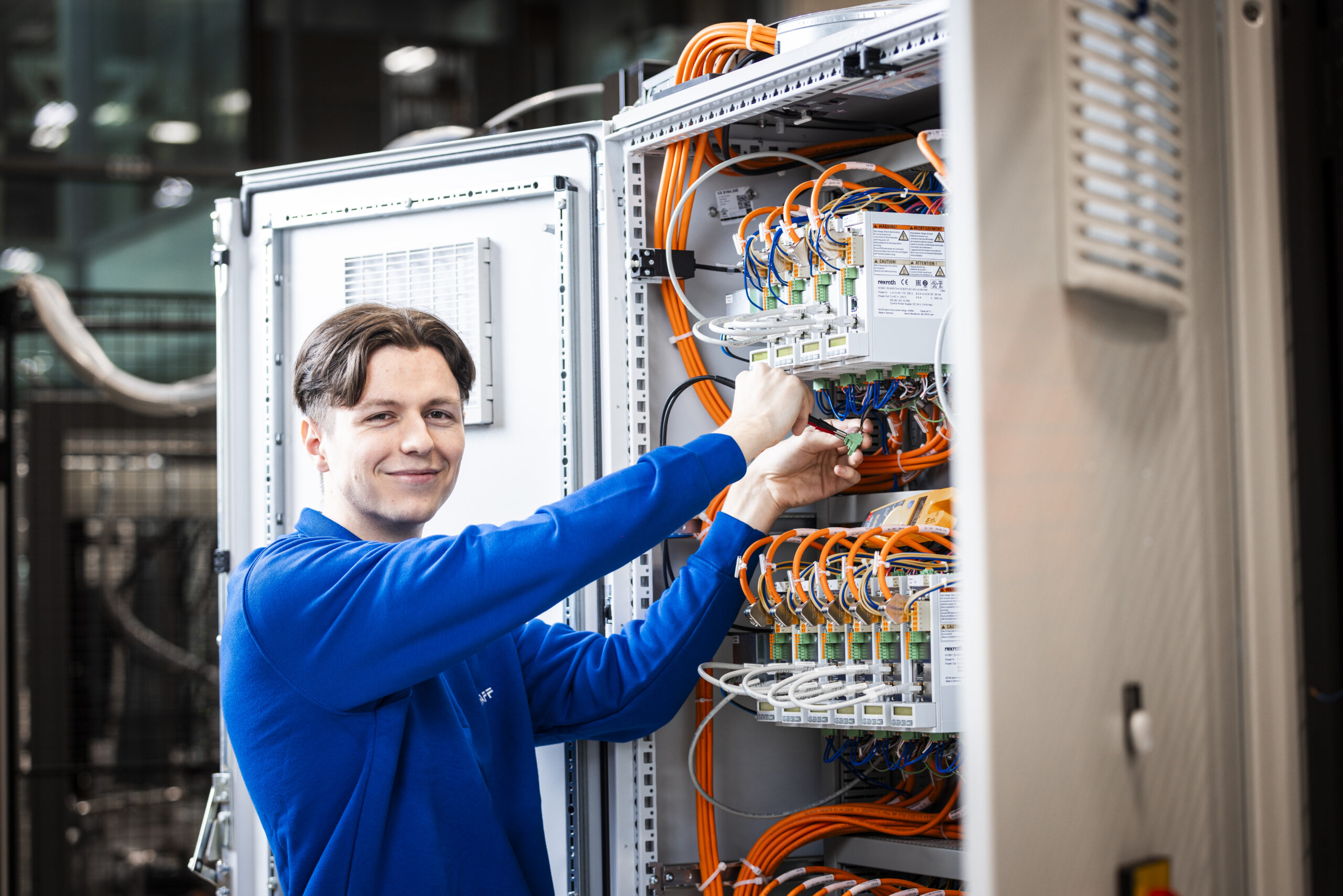 Employee smiling while working on a control cabinet and looking at the camera